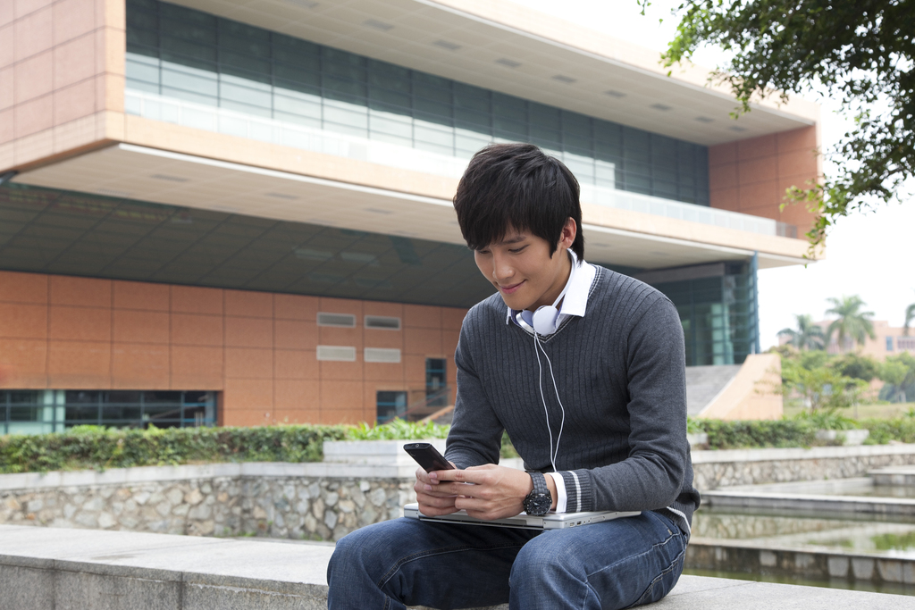 年轻男大学生在校园里使用笔记本电脑听音乐图片