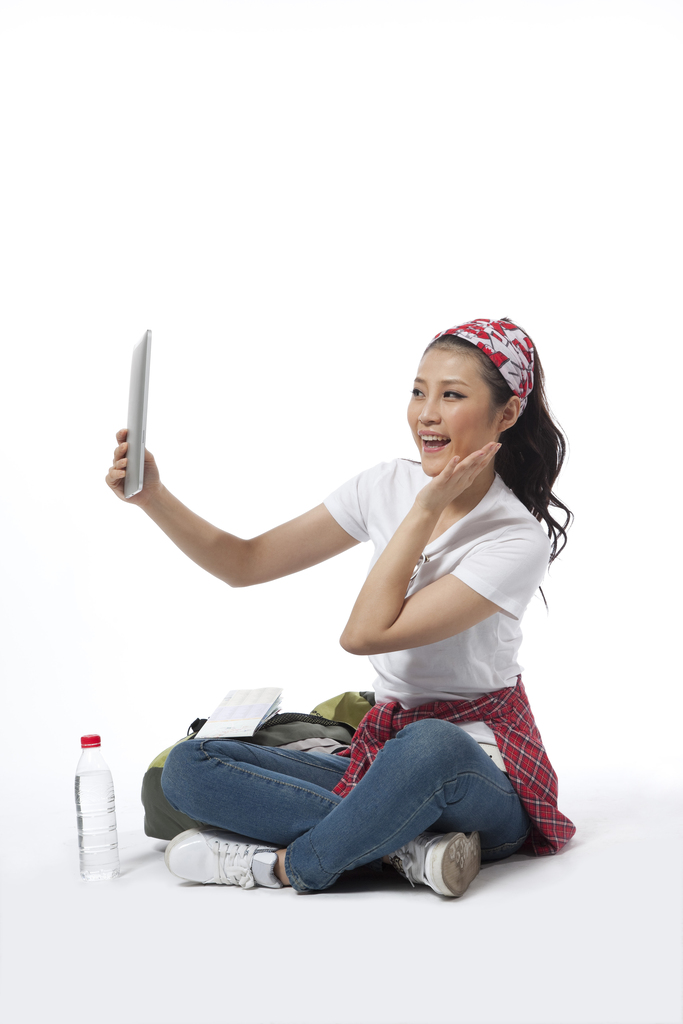 棚拍户外旅行的年轻女人坐在地上玩平板电脑