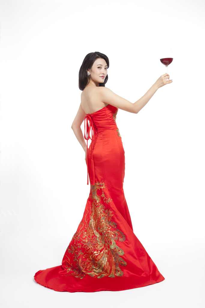 棚拍穿红色礼服的年轻女人端着红酒杯