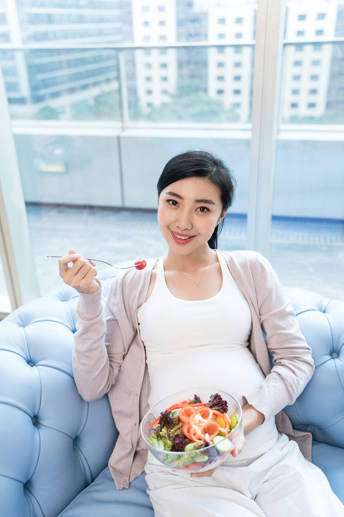 年轻孕妇坐在沙发上吃沙拉图片