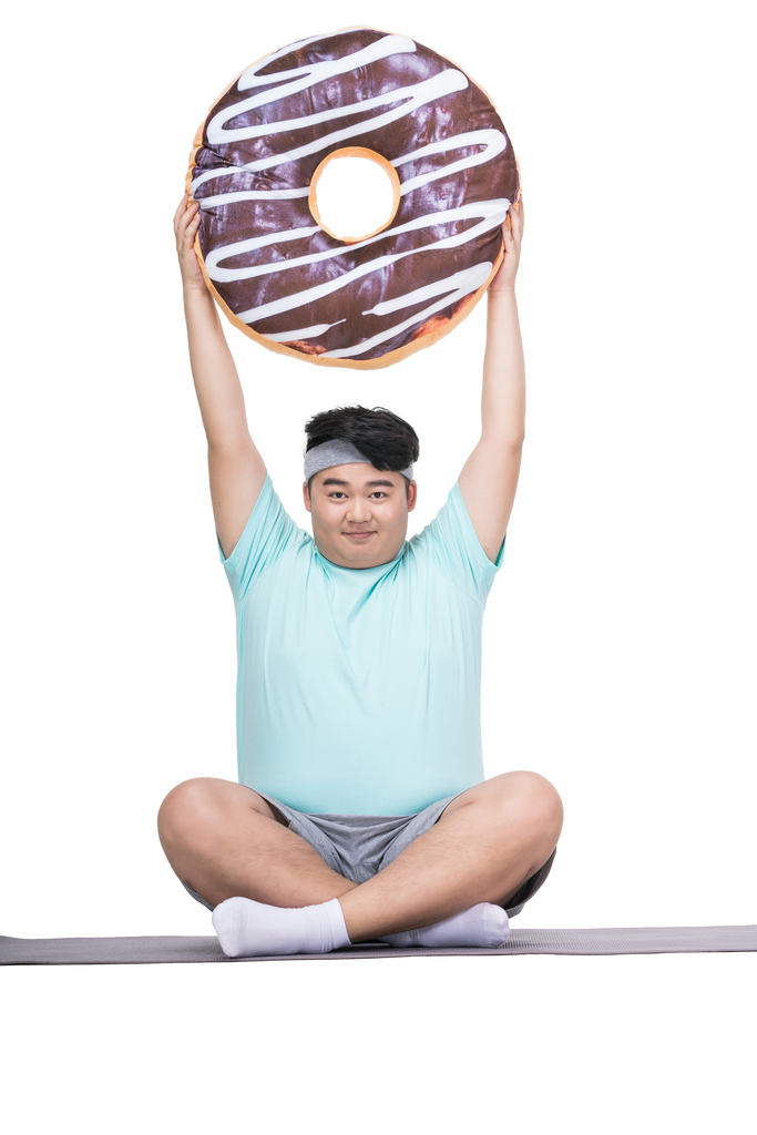 肥胖的青年男子拿着甜甜圈做运动