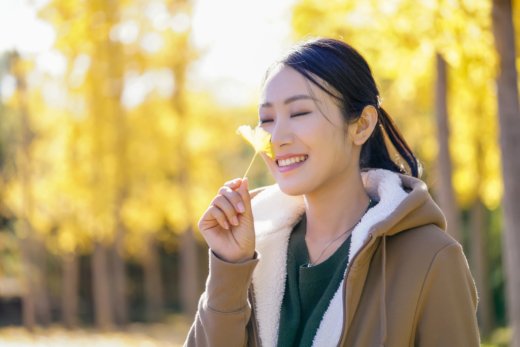 快乐的年轻女子手拿银杏叶图片