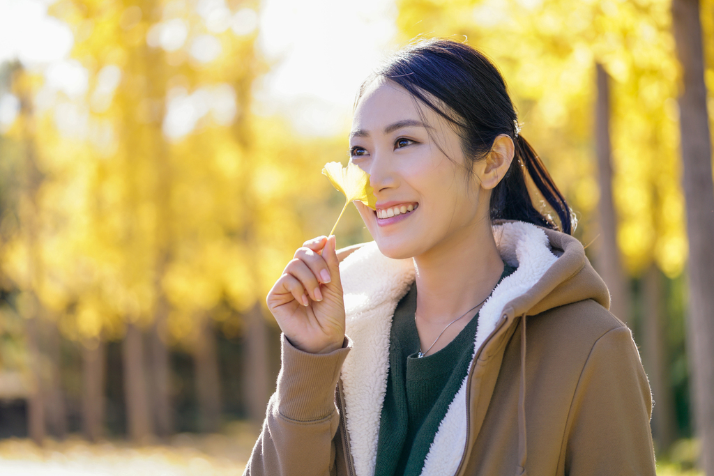 快乐的年轻女子手拿银杏叶图片