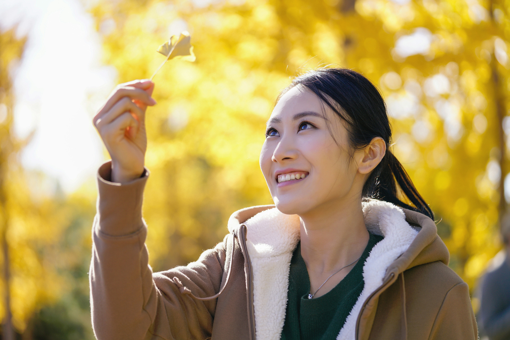 快乐的年轻女子手拿银杏叶图片