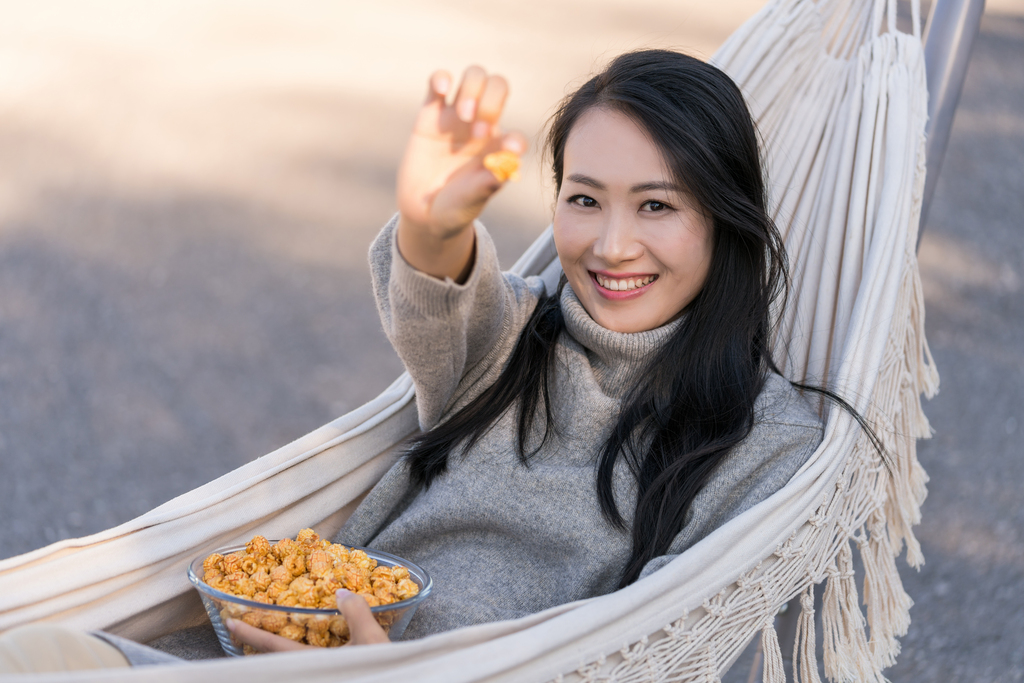 年轻女子坐在吊床上吃爆米花