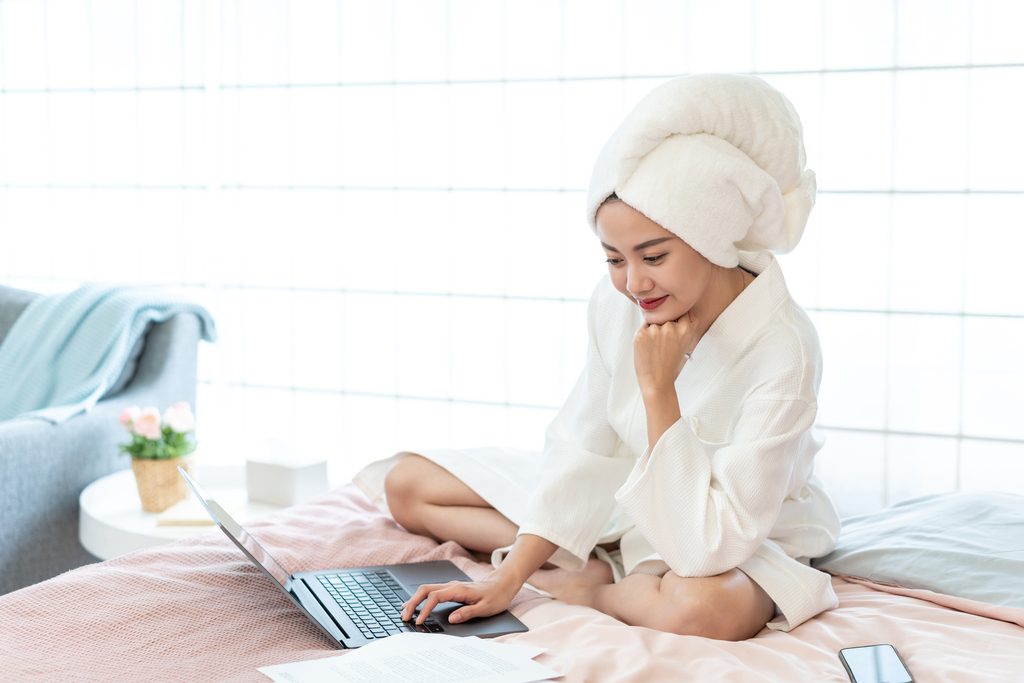 年轻女子穿着浴袍在床上使用电脑