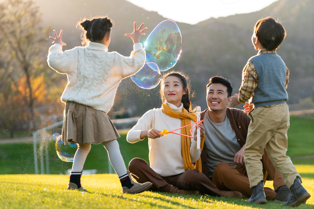 年轻夫妻和孩子们在草地上玩泡泡图片