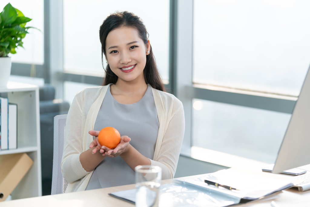 年轻女子在办公室拿着一个橙子