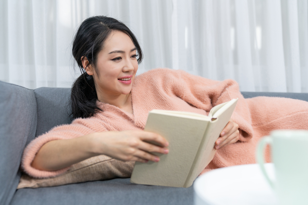 年轻女子躺在沙发上看书