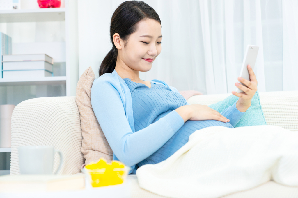 年轻孕妇在沙发上使用手机图片