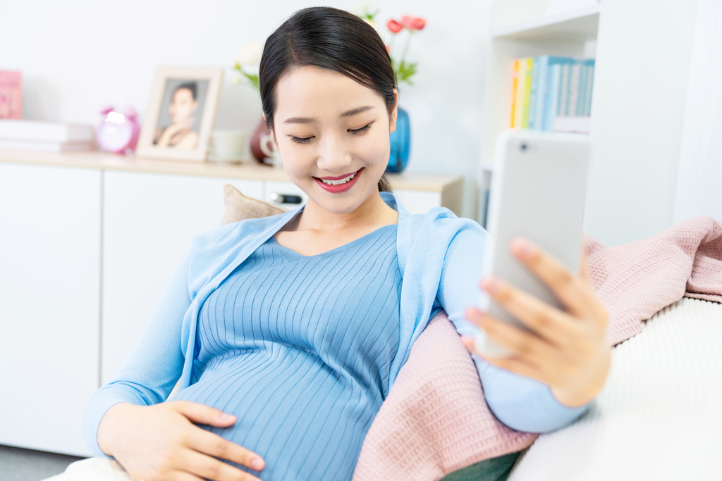 年轻孕妇在沙发上使用手机