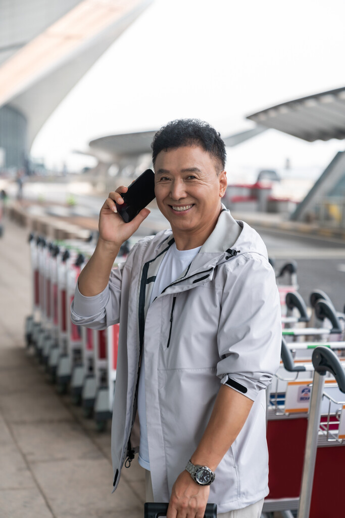 老年男人在机场拉着行李箱打电话