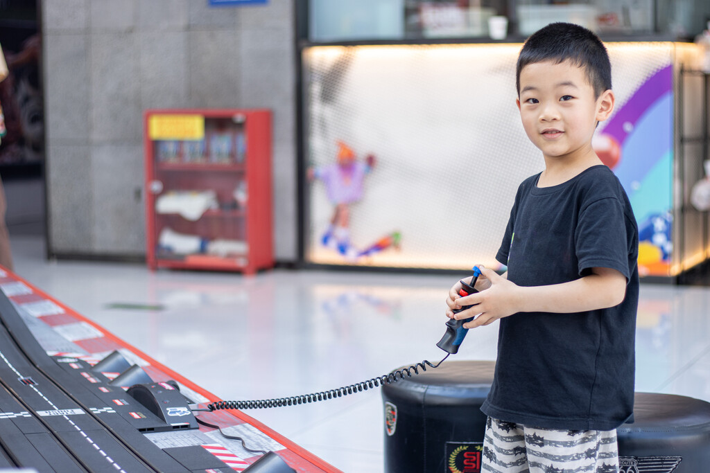 一个小男孩在游戏厅玩赛车玩具图片