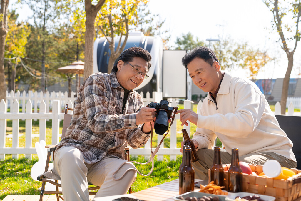 两个老年男人坐在露营地看数码相机图片