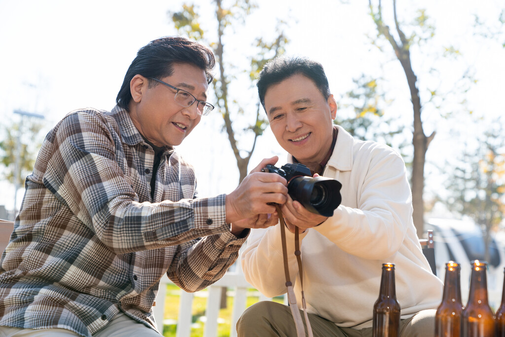 两个老年男人坐在露营地看数码相机图片