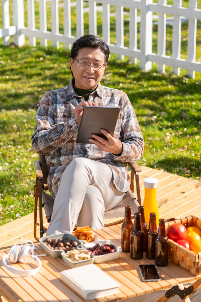 一个老年男人坐在露营院子里看平板电脑