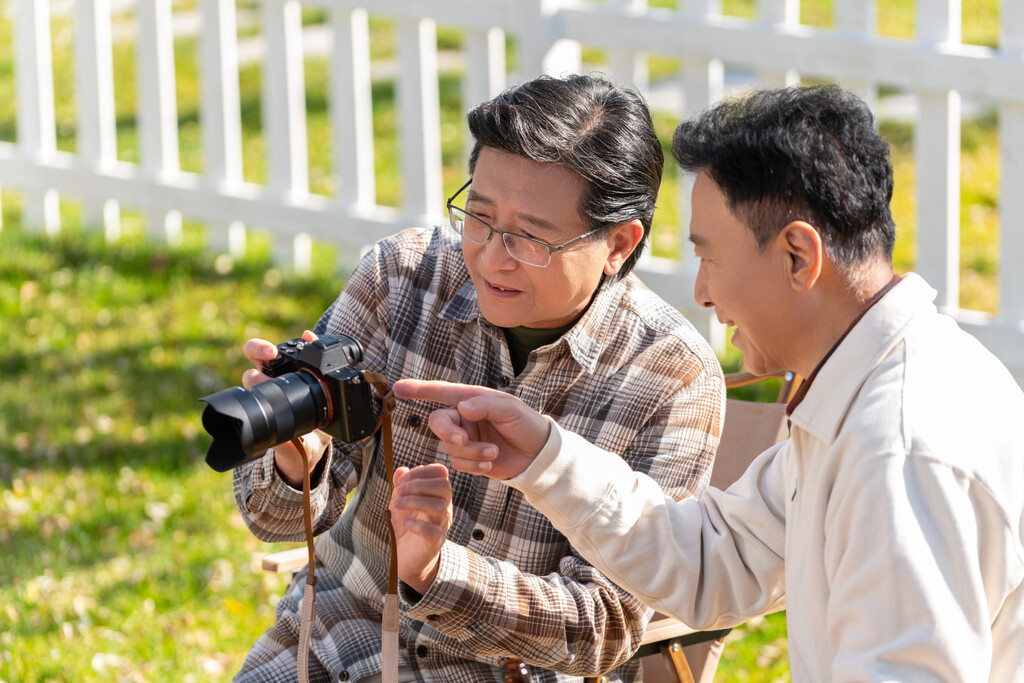 两个老年男人坐在露营地看数码相机