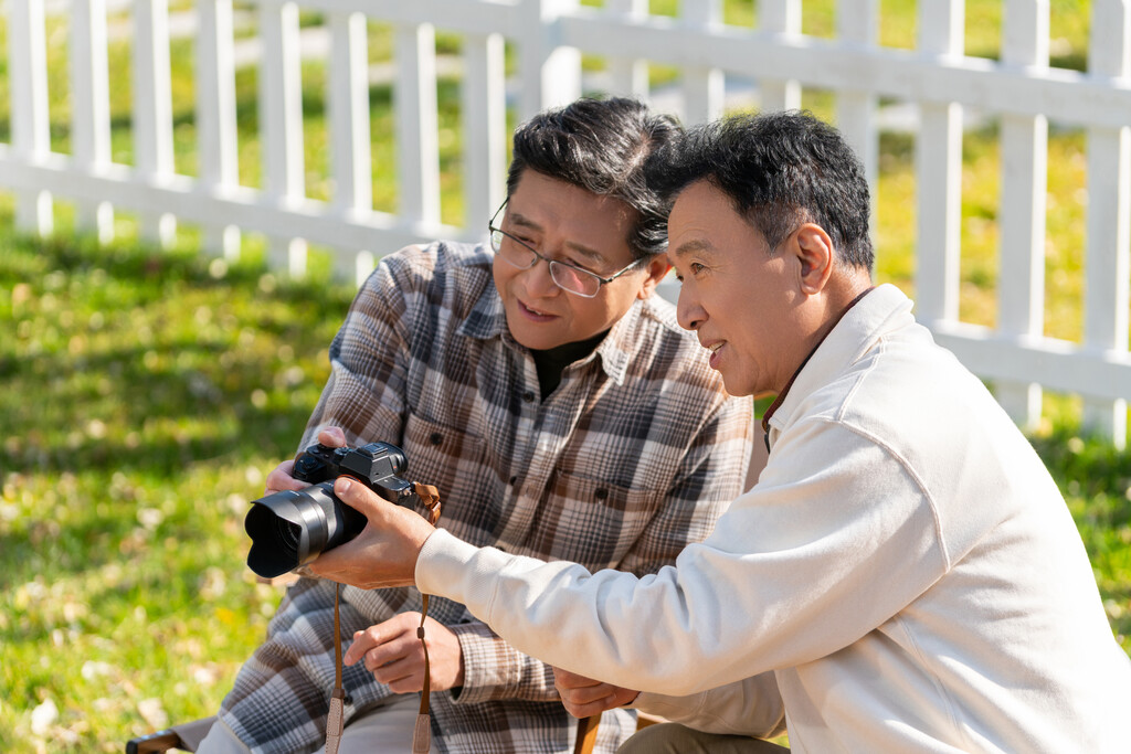 两个老年男人坐在露营地看数码相机